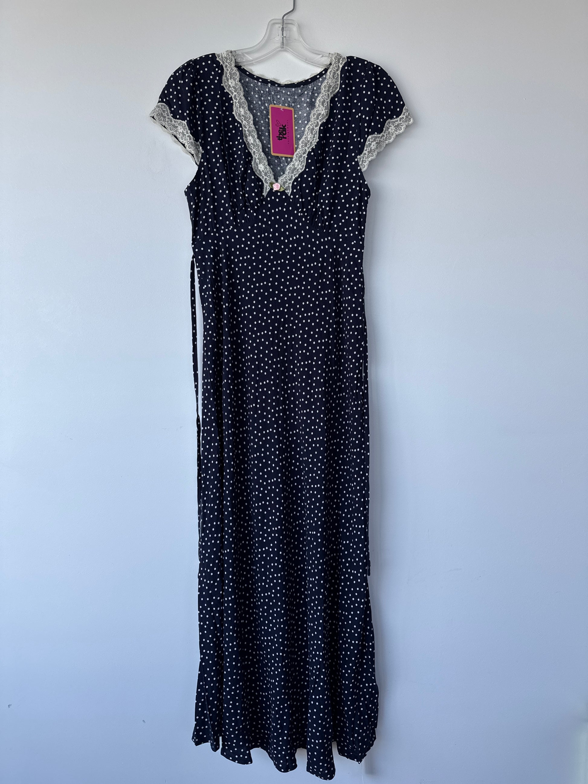 A black maxi dress with a white polka dot pattern, featuring a lace-trimmed V-neckline and short sleeves, hanging on a white hanger against a plain light gray wall.sherwood park secondhand, preloved, consignment, edmonton