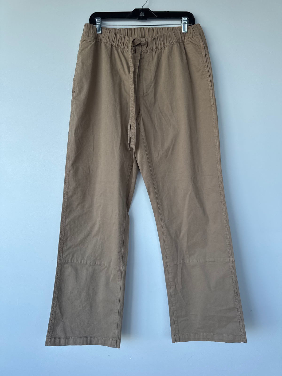 A pair of light brown or khaki drawstring pants hanging on a black hanger against a light blue wall. edmonton consignment, sherwood park consignment, secondhand, preloved, yeg, shpk
