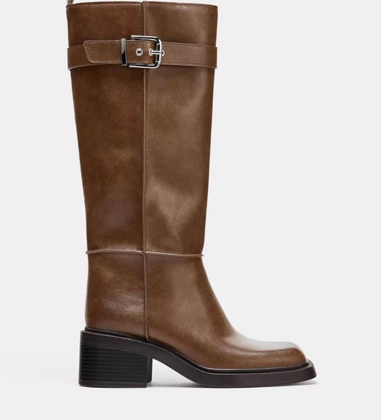 A brown leather knee-high boot with a black block heel and a silver buckle strap around the upper shaft, shown from a side profile on a light gray background. ZARA Topstitch boots, Zara knee-high boots, brown knee-high boots, lined knee-high boots, lined brown boots, women’s knee-high boots, square toe boots, square toe knee-high boots, chunky heel boots, low heel boots, buckle boots, brown fall boots, fall boots women, winter boots women, warm winter boots, Zara brown boots, dress boots, everyday boots, Sh
