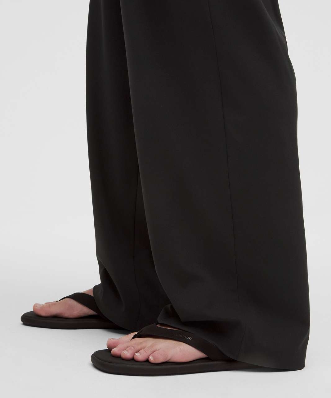 Black flat thong sandals worn with black wide-leg trousers, shown from the side against a light gray studio background. Lululemon pants. Sherwood Park consignment, Sherwood Park shopping, consignment store Sherwood Park, Edmonton consignment, secondhand shopping, secondhand clothing, women’s consignment, women’s clothing consignment, curated consignment, quality secondhand clothing, pre-loved clothing, thrift shopping, sustainable fashion, local shopping, Alberta consignment