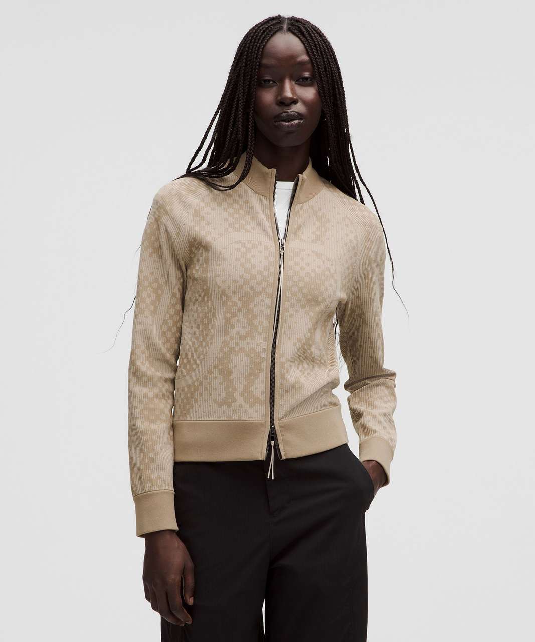 A model wearing a beige patterned zip-up bomber jacket with black trousers, photographed against a solid light gray background. RARE LULULEMON. Sherwood Park consignment, Sherwood Park shopping, consignment store Sherwood Park, Edmonton consignment, secondhand shopping, secondhand clothing, women’s consignment, women’s clothing consignment, curated consignment, quality secondhand clothing, pre-loved clothing, thrift shopping, sustainable fashion, local shopping, Alberta consignment
