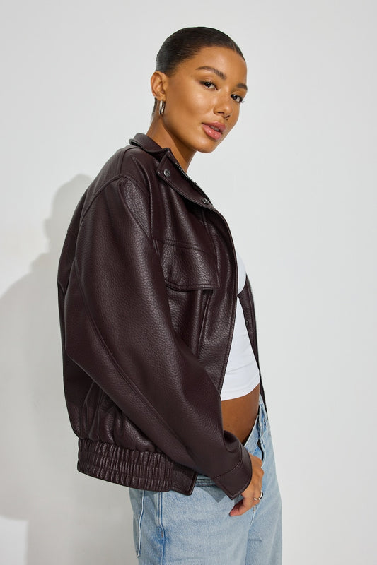 A woman wearing a dark brown faux-leather jacket, styled with a white crop top and light blue jeans, photographed against a plain light gray studio background. Sherwood Park consignment, Sherwood Park shopping, consignment store Sherwood Park, Edmonton consignment, secondhand shopping, secondhand clothing, women’s consignment, women’s clothing consignment, curated consignment, quality secondhand clothing, pre-loved clothing, thrift shopping, sustainable fashion, local shopping, Alberta consignment