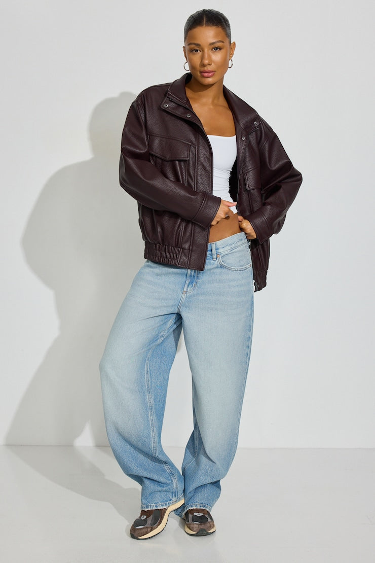 A model wearing a dark wine coloured faux-leather cropped jacket, light-wash wide-leg jeans, and brown sneakers, standing against a light gray studio wall. Sherwood Park consignment, Sherwood Park shopping, consignment store Sherwood Park, Edmonton consignment, secondhand shopping, secondhand clothing, women’s consignment, women’s clothing consignment, curated consignment, quality secondhand clothing, pre-loved clothing, thrift shopping, sustainable fashion, local shopping, Alberta consignment. Garage. 