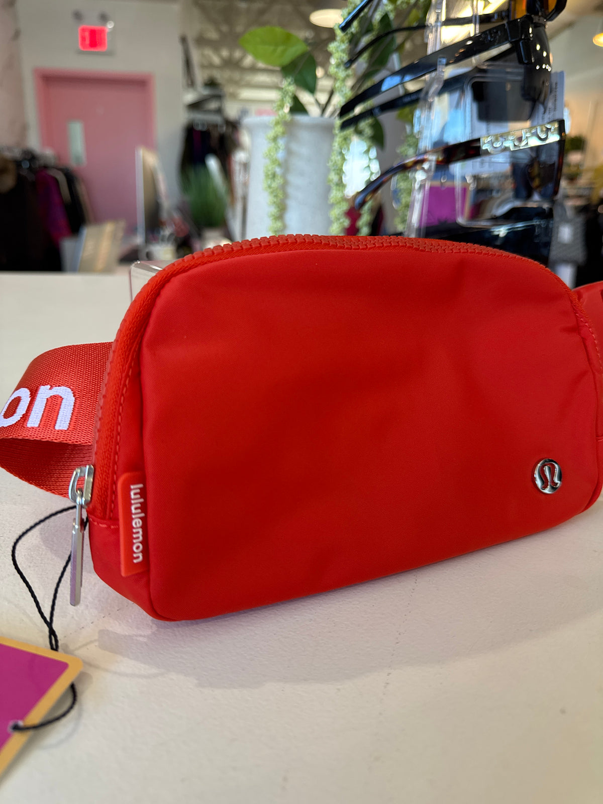A bright red Lululemon waist bag with a matching red strap featuring white lettering, resting on a white counter in a retail store.