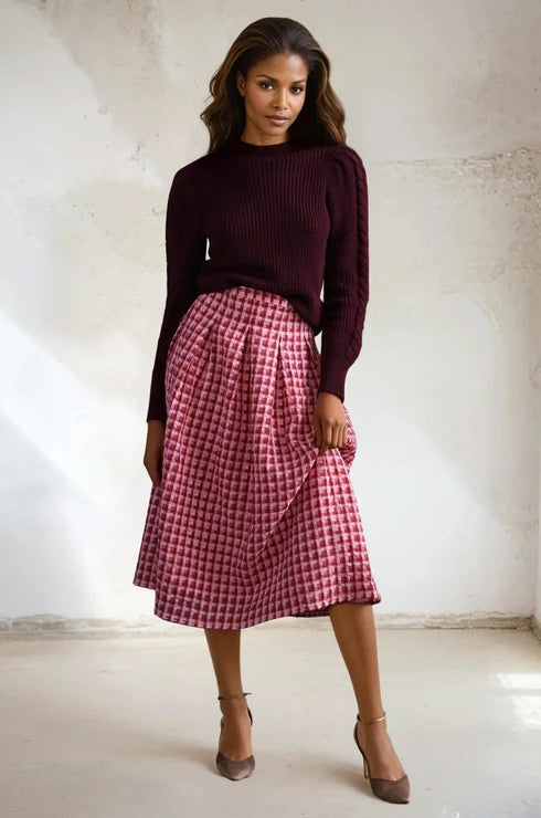 Woman wearing a burgundy sweater and pink checkered skirt against a white background. Anthropologie consignment, consignment store, thirft shop