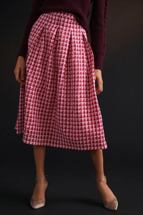 A model wearing a red and white gingham pleated midi skirt, paired with a dark burgundy sweater and beige pointed-toe heels, set against a dark studio background. Anthropolgie skirt, secondhand premium clothing, Alberta
