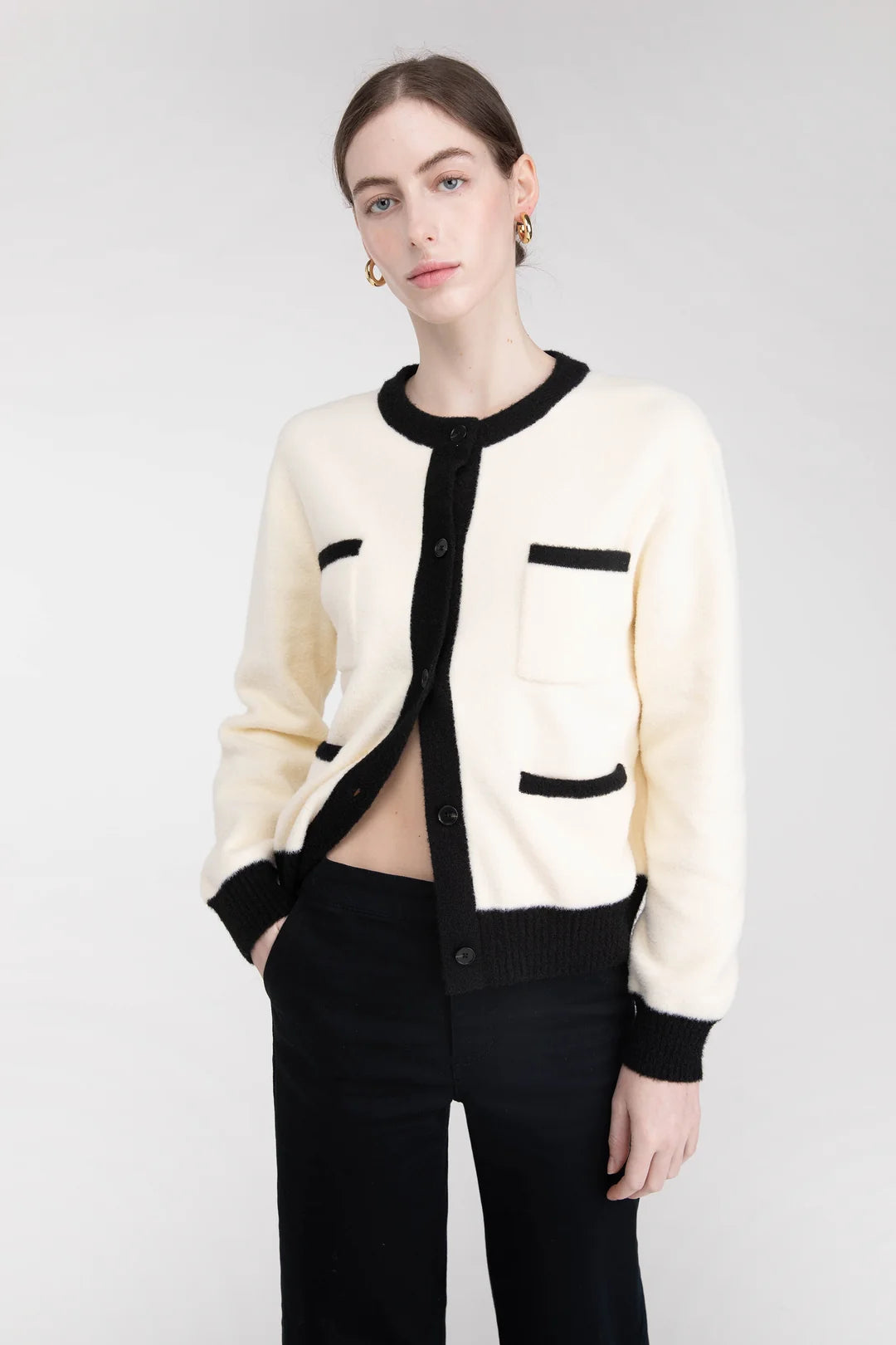 A model wearing a cream-colored Oak + Fort cardigan with black trim and black pants, photographed against a neutral light gray studio background. Sherwood Park consignment